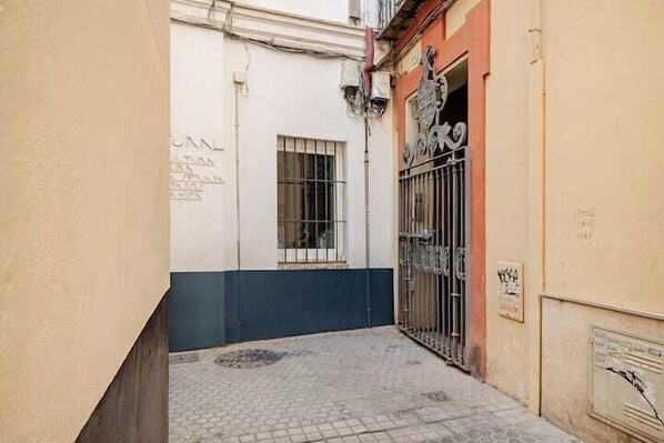 A narrow alleyway with a tiled floor, a window with metal bars, and a gated entrance with a sign. - Boutique Abades Apartment I (Seville)
