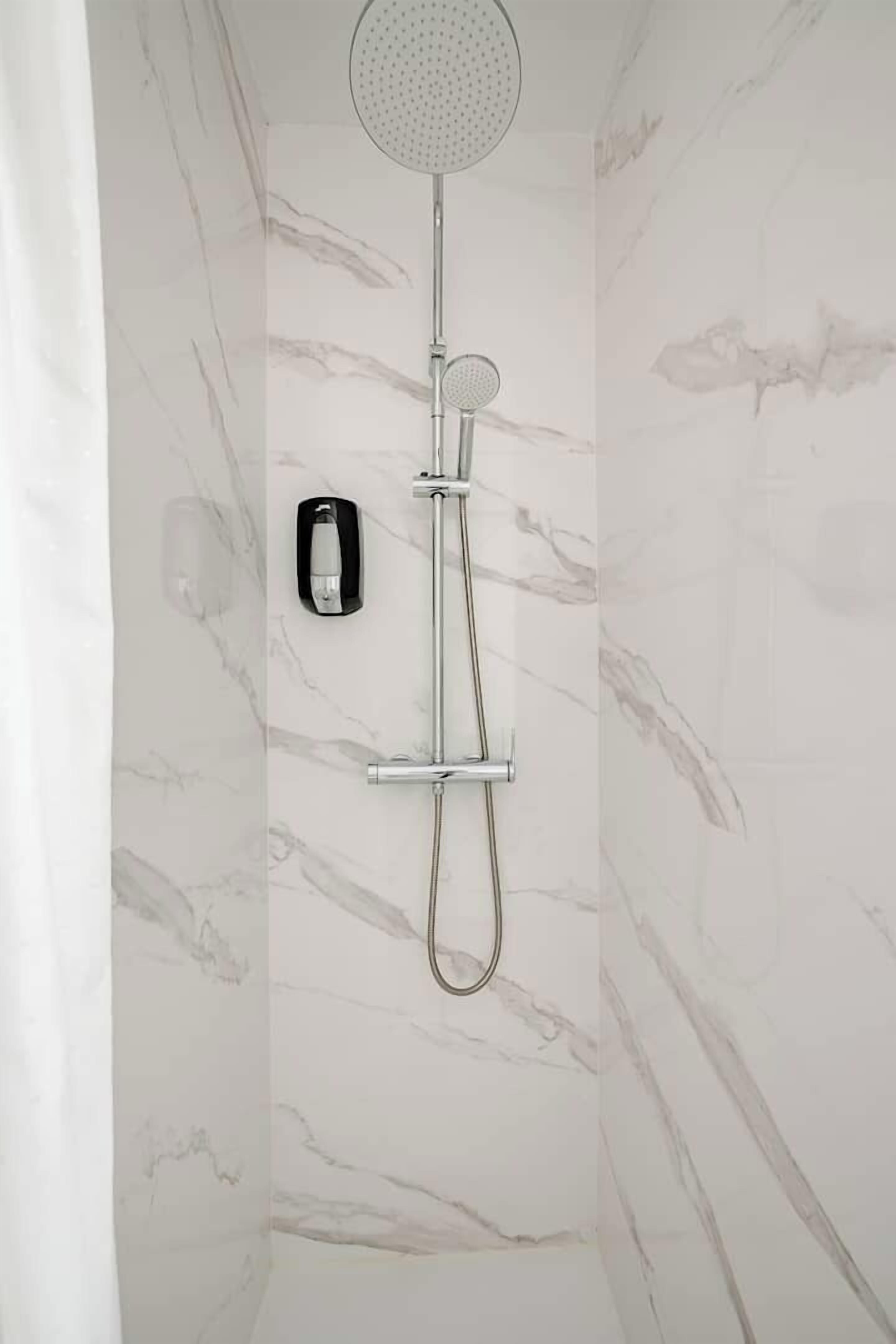 A shower with a handheld showerhead and a wall-mounted faucet, set against a marble wall.