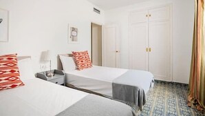 Ett hotellrum med två sängar, en takfläkt, en garderob och ett mönstrat golv.