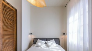 Un letto rifatto con cura, una testiera, due abat-jour e una finestra con tende leggere.