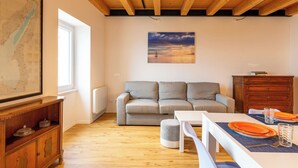 Ein Wohnzimmer mit Holzboden, einer Couch, einem Esstisch mit orangefarbenen Tellern und einer Holzkommode.