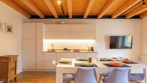 Eine moderne Küche mit Holzbalken, einem Flachbildfernseher und einem Essbereich mit Stühlen und Geschirr.