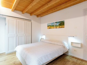 Une chambre avec un plafond en bois, un lit avec une literie blanche, une armoire blanche et un tableau accroché au mur.