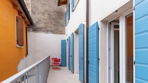 A narrow corridor with blue doors, a small table with red chairs, and a white railing. - l'Isola by Interhome (Brenzone)