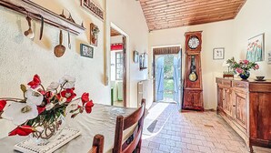 A dining area with a table set for two, a wooden bench, a clock, and a view of the garden through an open door. - L'Agapanthe by Interhome (Pornic)
