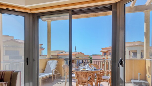 Un balcon avec une table dressée pour deux personnes, des chaises en osier et une vue sur les immeubles voisins.