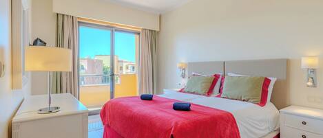 A hotel room with a large bed, a bedside table, a lamp, and a view of buildings through a window.