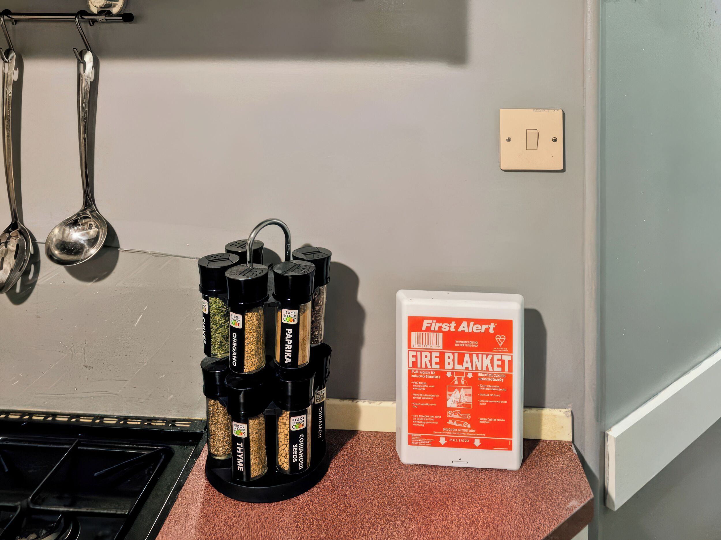 Une cuisine équipée d’un étagère à épices, d’une couverture anti-feu et d’un interrupteur fixé au mur.