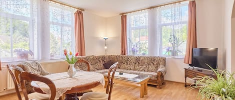 A living room with a sofa, a coffee table, a TV, and a dining table with chairs.