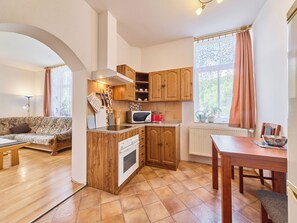 A compact kitchen with wooden cabinets, a microwave, and a stove. There's a dining table and a sofa in the adjacent living area.