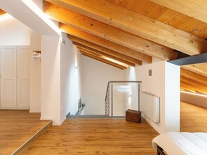 Une pièce avec un plafond en pente, des poutres en bois, un radiateur, une valise et un lit.