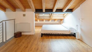Ein Schlafzimmer mit Holzbalkendecke, einem Bett, einem Heizkörper und einem Koffer.