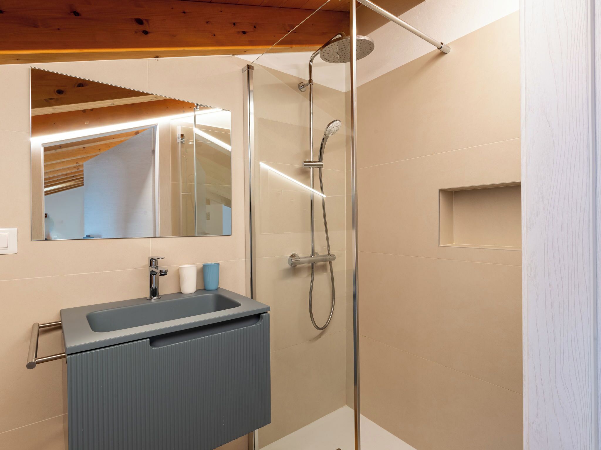 Ein modernes Badezimmer mit Duschkabine aus Glas, Waschbecken und Spiegel sowie Holzboden.