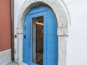 Une porte bleue dotée d’un clavier pour l’ouverture, un cadre en pierre en forme d’arc et un tuyau métallique sur le côté gauche.