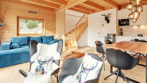 Un interior moderno de cabaña de troncos con un sofá azul, una mesa de comedor y sillas.