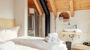 Un dormitorio con una cama grande, techo de madera, baño con lavamanos y espejo, y zona de ducha.