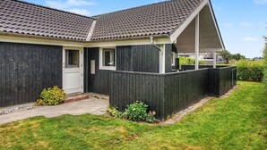 A single-story house with a dark wooden exterior, a tiled roof, and a small front yard with a white door and windows. - "Lanica" - 150m from the sea by Interhome (Mesinge)