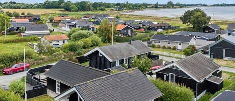 A residential area with houses, a red car, and a body of water in the background.