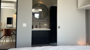 A modern bedroom with a large bed, a round mirror, a built-in desk with a chair, and a bathroom with a sink and mirror. - De Zeebries by Interhome (Scherpenisse)