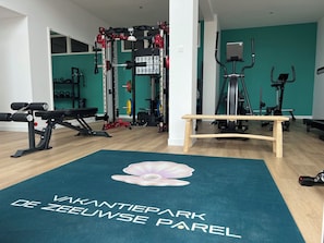Une salle de sport avec un banc en bois, du matériel de musculation et un mur de couleur turquoise.