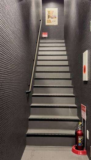 Un escalier avec des murs noirs et un extincteur sur le côté droit.