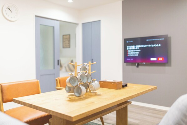A room with a wooden table, chairs, a clock, and a TV displaying Japanese text. - b&Kishinosato (Osaka)
