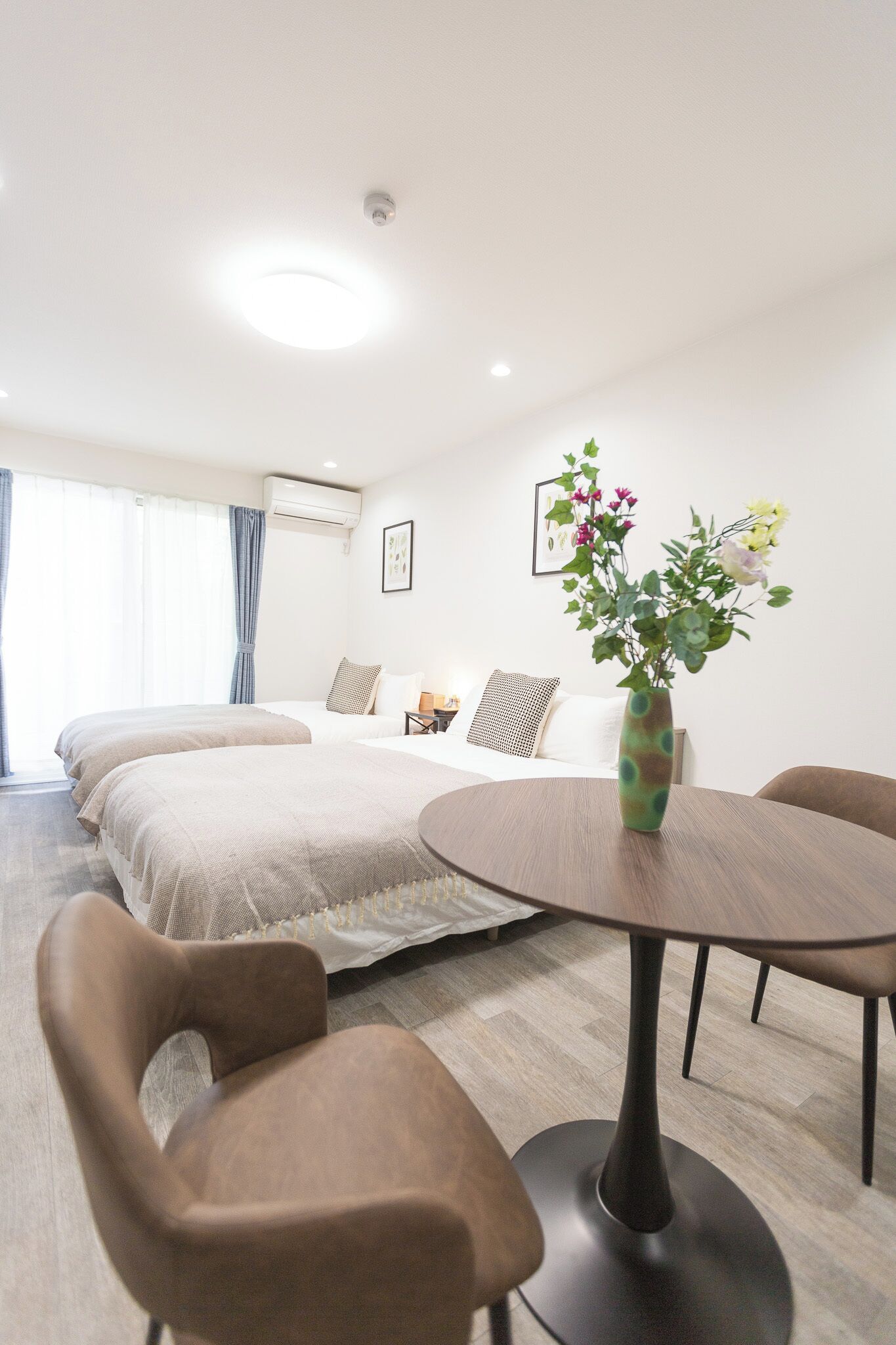 Una habitación de hotel con una cama, una mesa redonda y un florero con flores.