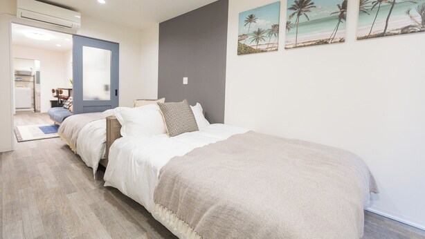 A bedroom with a large bed, a dresser, and a door leading to a bathroom. - b&Kishinosato (Osaka)
