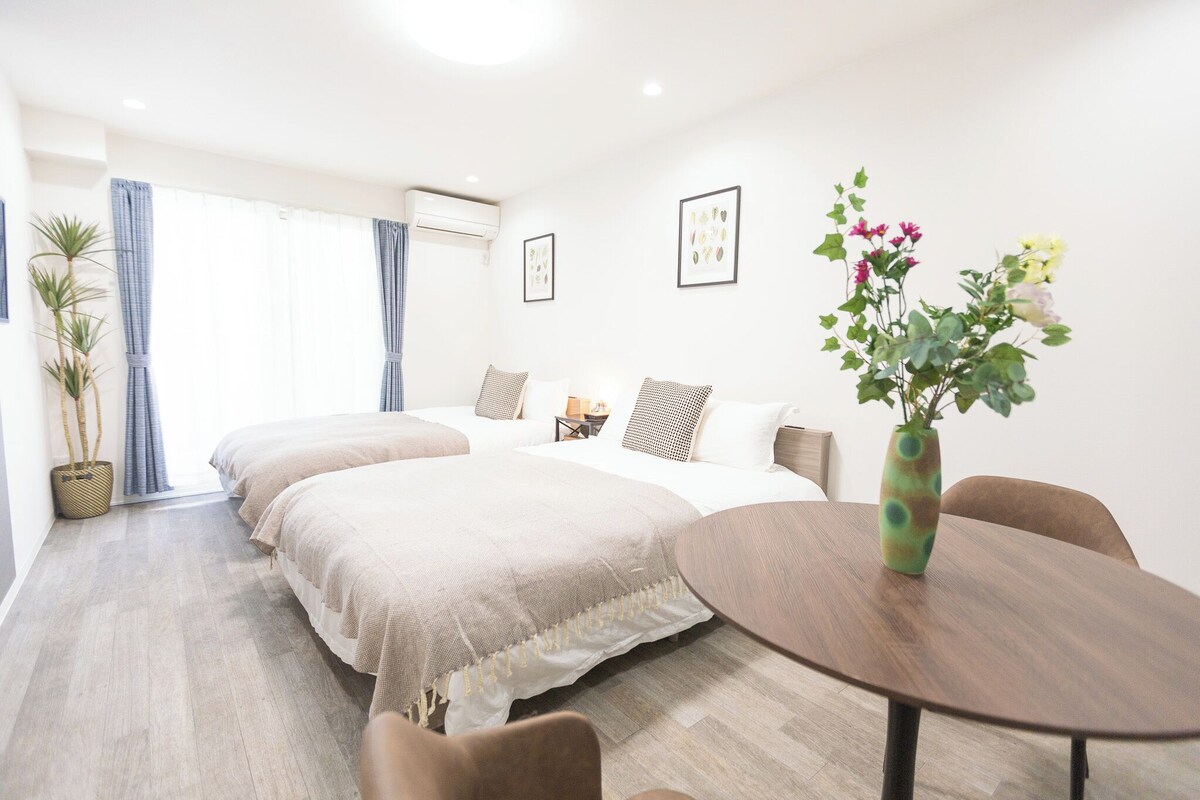 A hotel room with two beds, a dining table, and a vase of flowers.