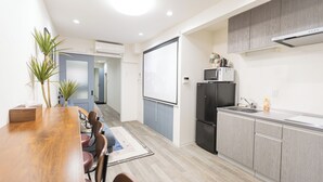 A modern kitchen with grey cabinets, a black refrigerator, and a microwave. There is a wooden dining table with chairs and a small plant on the left. - b&Kishinosato (Osaka)