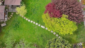 Vue plongeante d’un jardin avec un chemin de pierres, des arbustes de différentes couleurs et un bâtiment doté d’un toit brun.