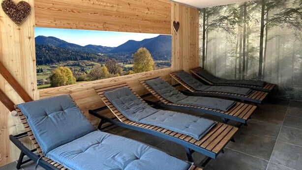 Une pièce dotée de quatre fauteuils inclinables, disposés face à une grande fenêtre offrant une vue sur des montagnes et une forêt.