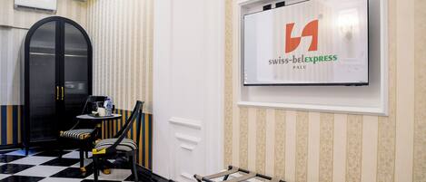 Un hall d'hôtel avec un sol à carreaux, un mur rayé de noir et de blanc, une porte noire incurvée et un écran affichant le logo de SwissExpress.