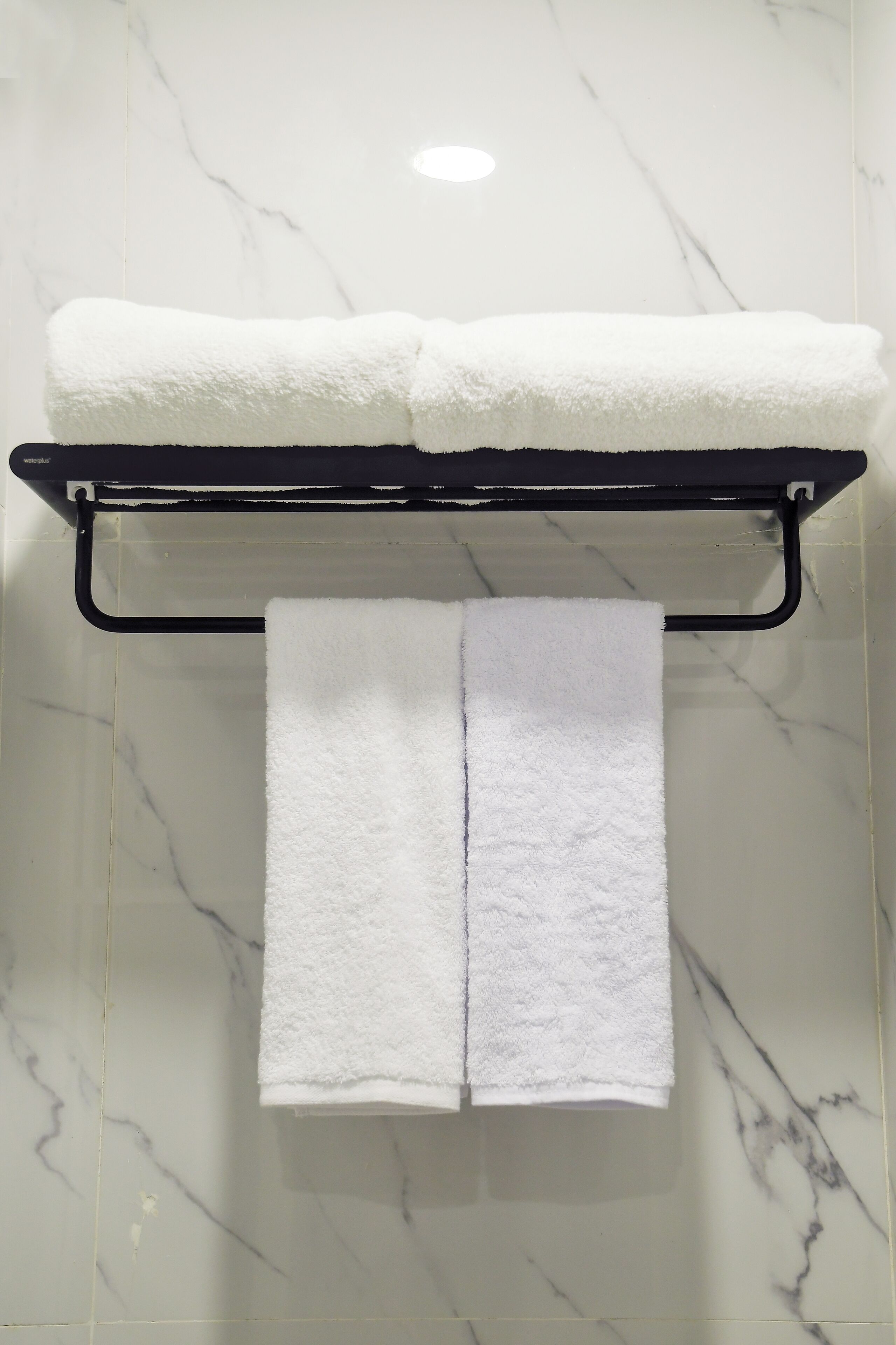 Un baño con piso de mármol, un toallero negro que sostiene dos toallas blancas, y una toalla blanca colgando debajo.