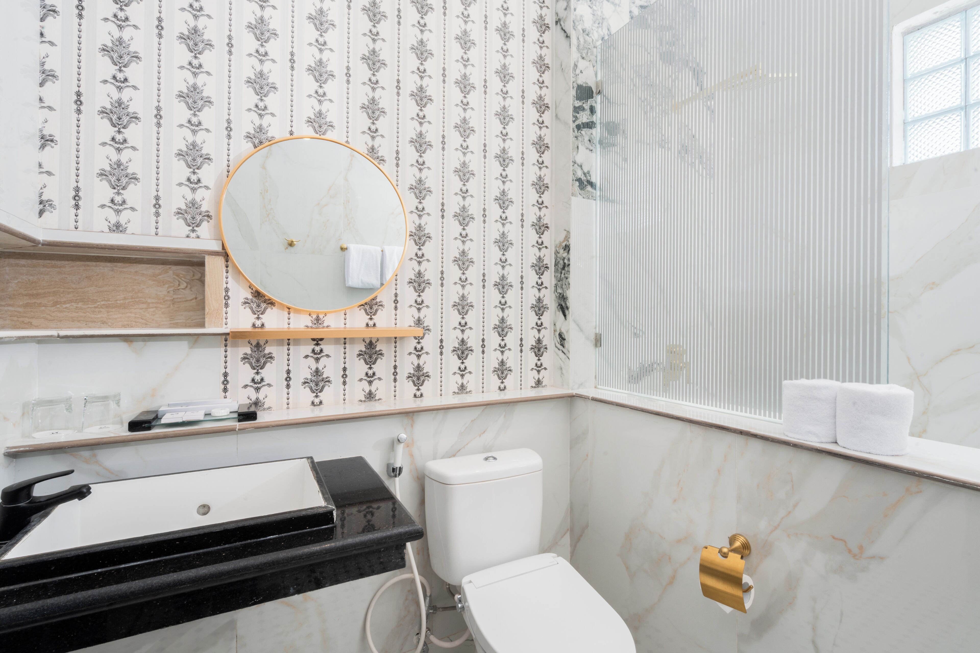 A bathroom with a marble sink, toilet, and a window with a view.