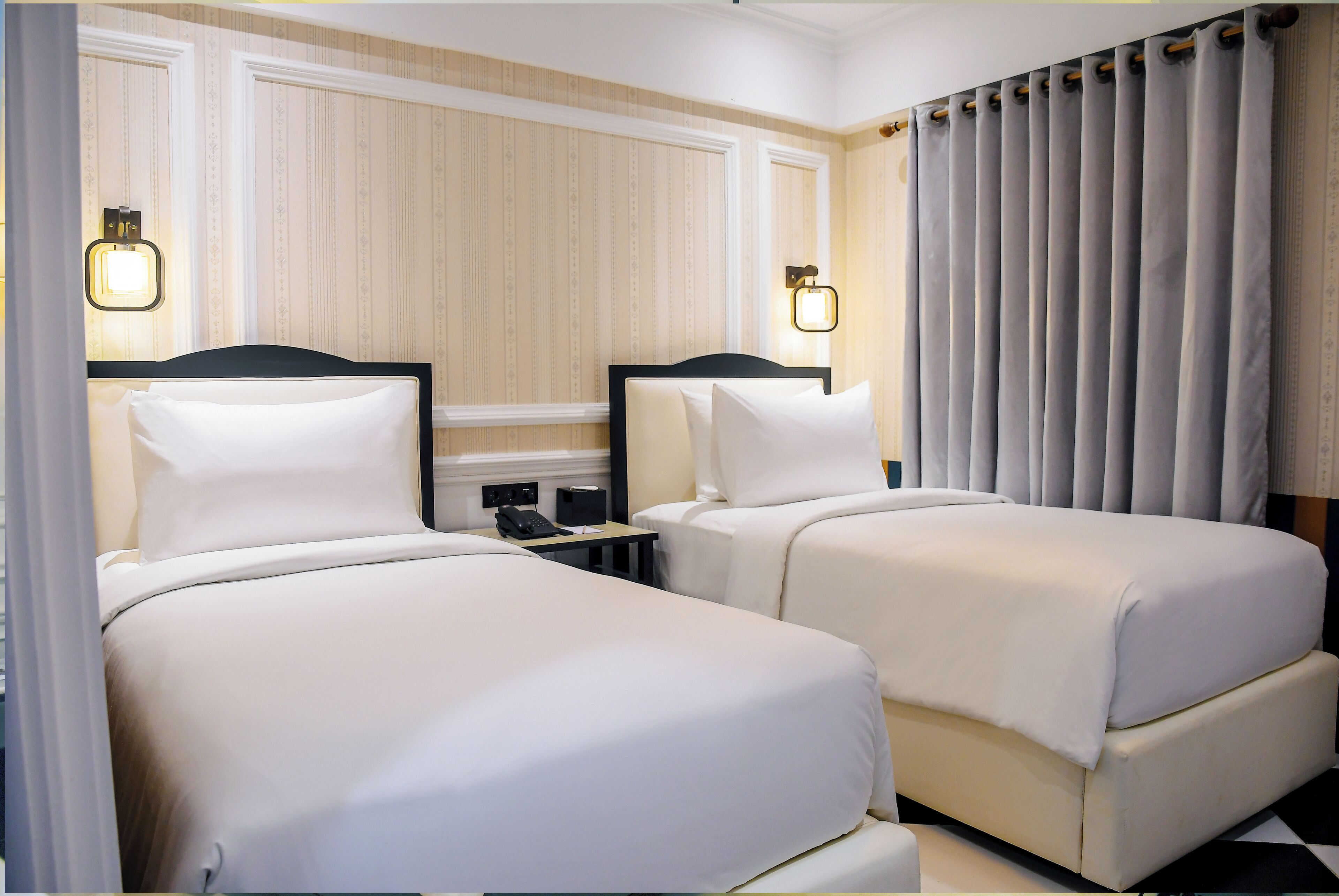 Habitació d'hotel amb dos llits, una taula de nit amb telèfon i una finestra amb cortines.