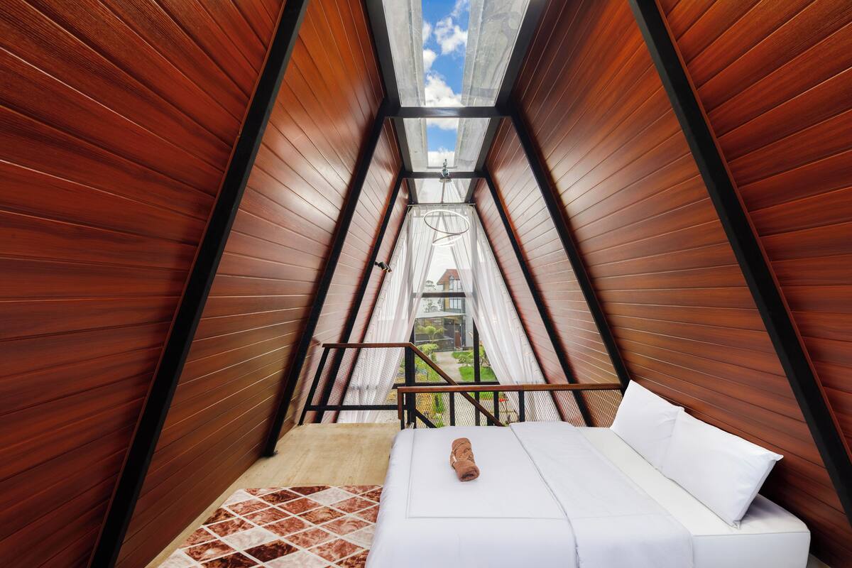 Ein schmales Zimmer mit Holzwänden und einer schrägen Decke, das zu einem Balkon mit Blick auf Grünflächen führt.