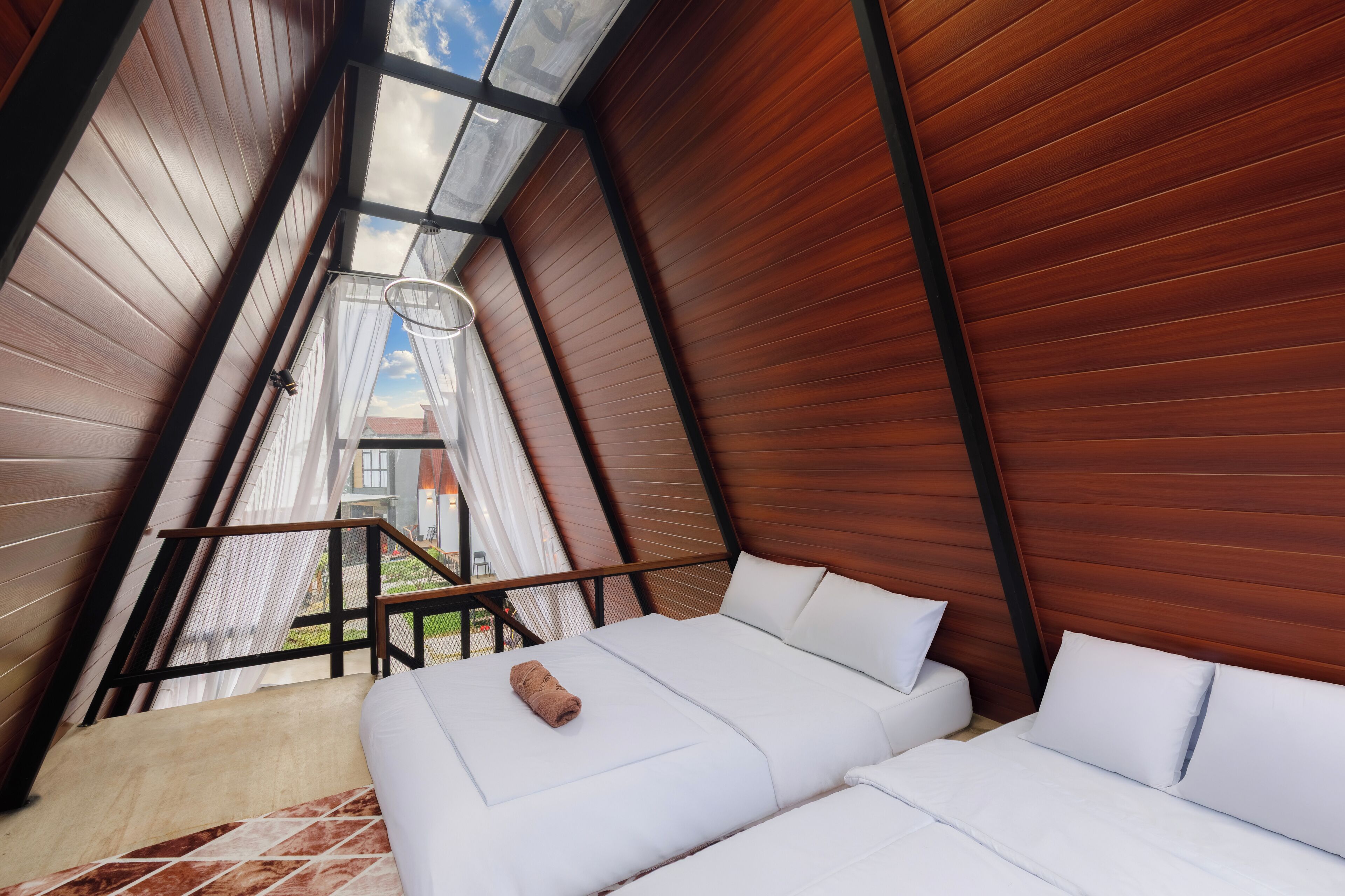 Een moderne, driehoekige kamer met een bed en uitzicht op buiten via een groot dakvenster.