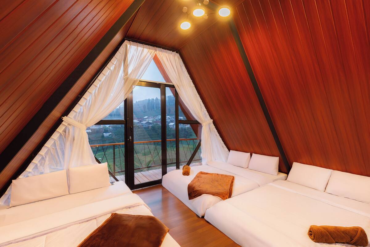 Ein gemütlicher, dreieckiger Raum mit großem Fenster, Holzwänden und einem Bett mit weißer Bettwäsche und braunen Kissen.