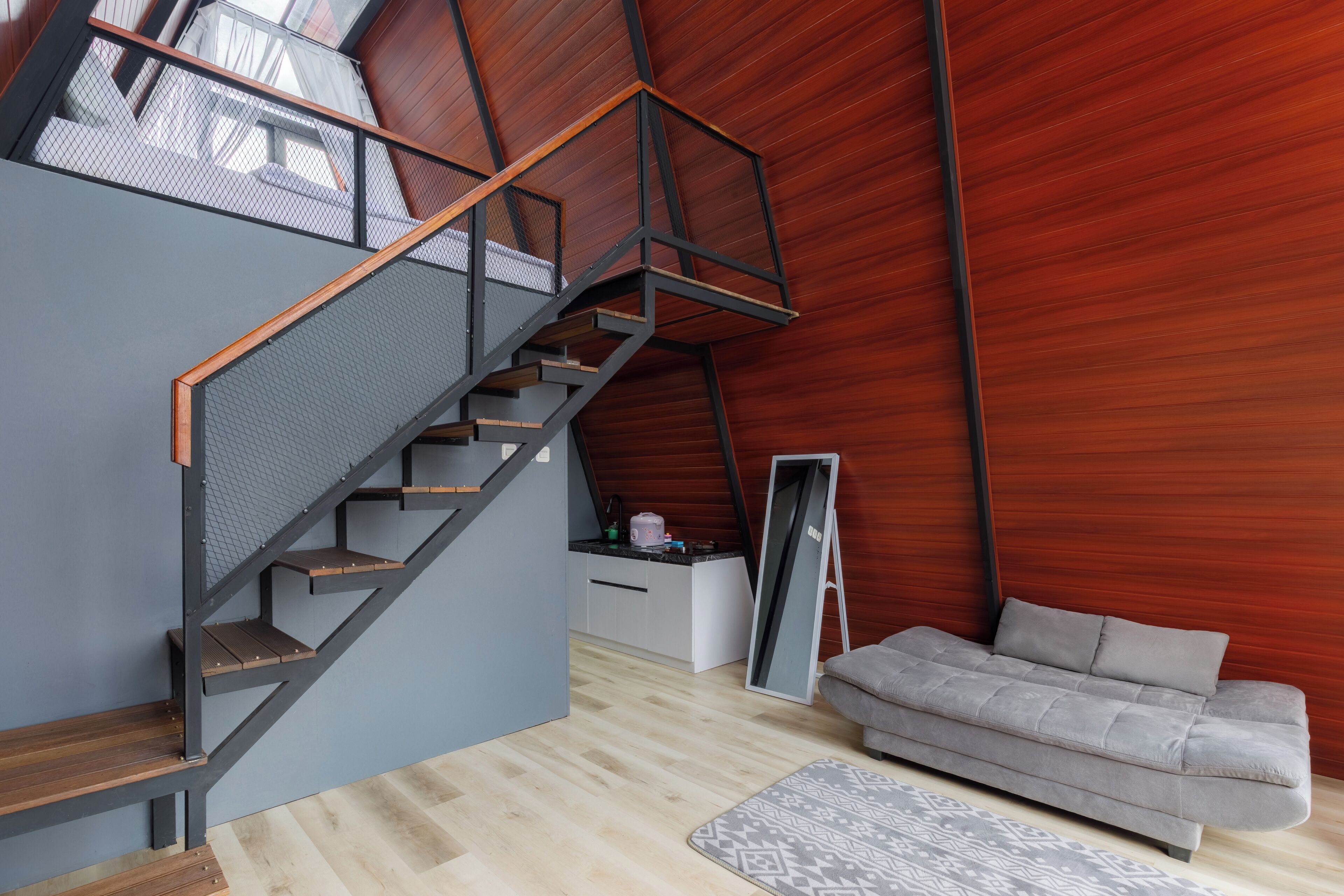 Quarto moderno estilo loft, com escada de madeira, sofá cinza e um espelho grande.