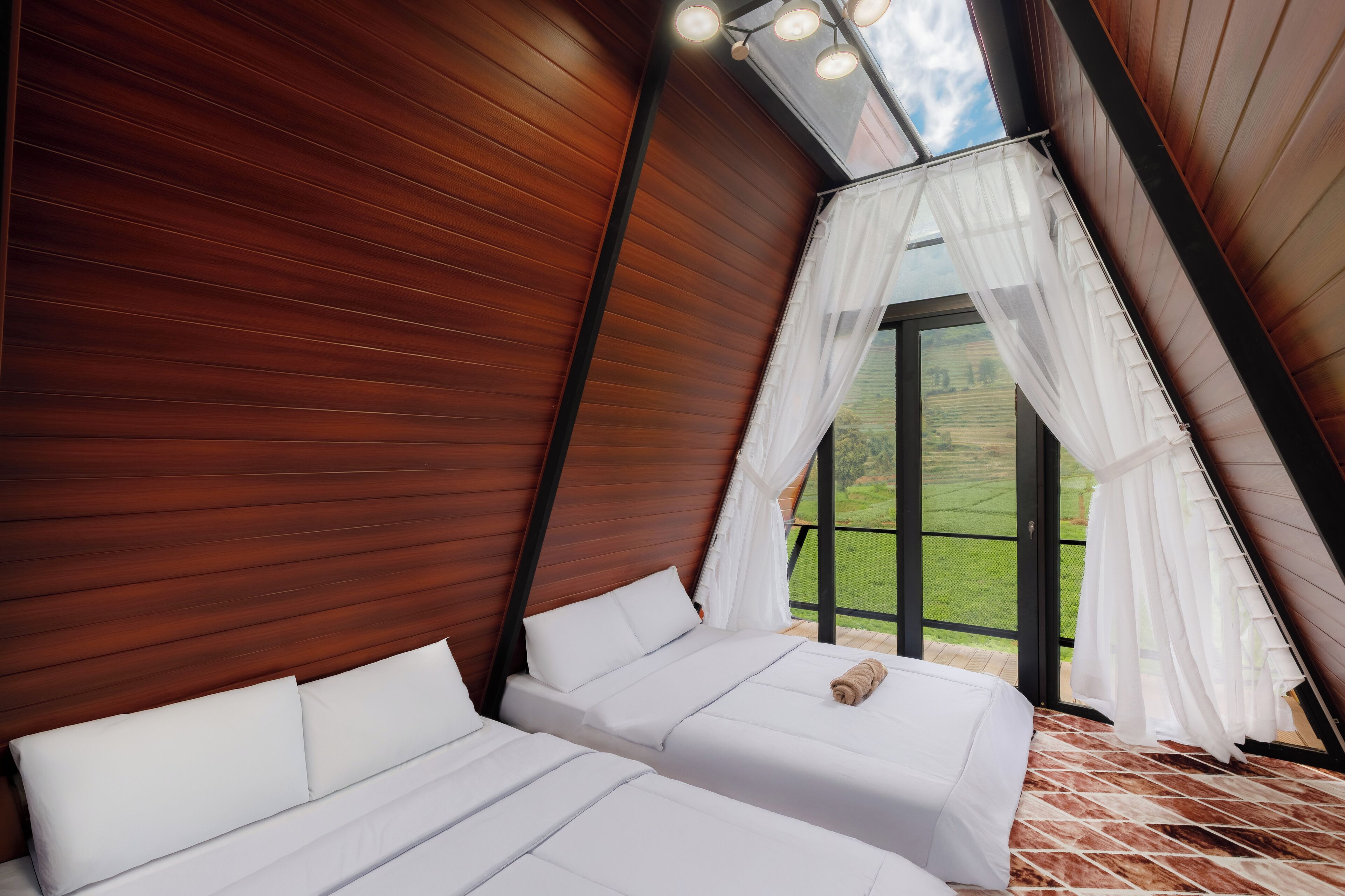 A bedroom with two beds, wooden paneling, a skylight, and a view of the outdoors.