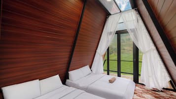 A bedroom with two beds, wooden paneling, a skylight, and a view of the outdoors.