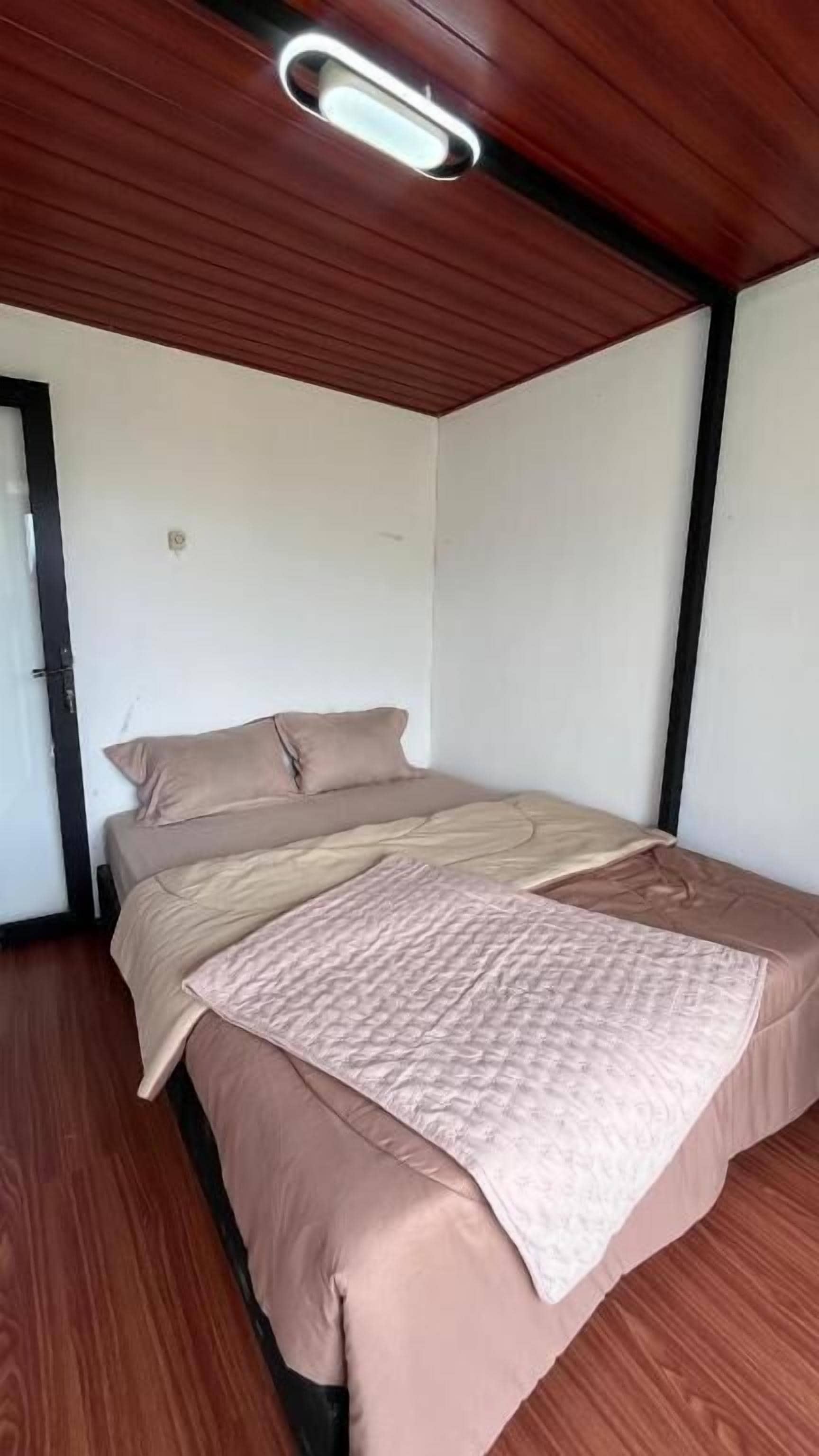 A bedroom with a wooden ceiling, a bed with beige bedding, and a white wall.