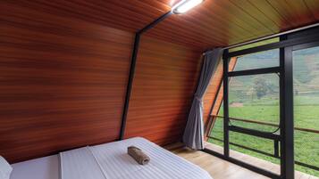 Un dormitorio con techo de madera, un ventanal con vistas a campos verdes y una toalla enrollada sobre la cama.