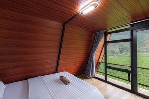 Un dormitorio con techo de madera, un ventanal con vistas a campos verdes y una toalla enrollada sobre la cama.