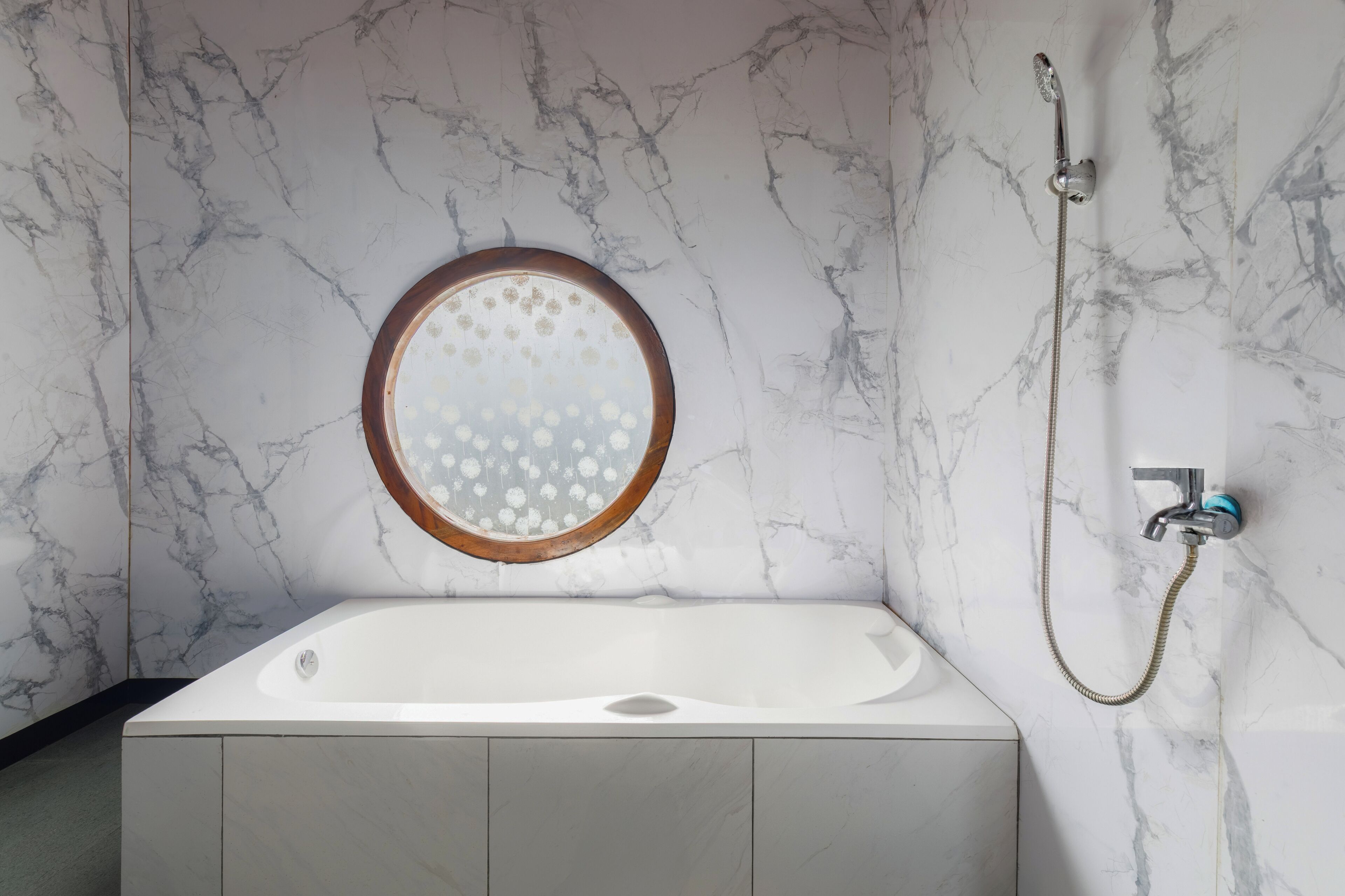 Een moderne badkamer met een marmeren wand, een ronde spiegel, een badkuip en een douche.