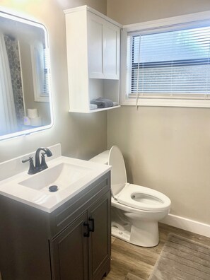 A bathroom with a white sink, dark cabinets, a toilet, and a window with blinds.