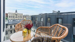 A balcony with wicker chairs and a table, a potted plant, and a glass table. - Lumina luxury apart with beautiful view (Łódź)