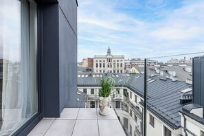 Un balcón con una planta en maceta, vista de un edificio histórico y cielo despejado.