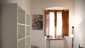 Ein Eckzimmer mit Heizkörper, Holzschrank, Stuhl und einem Blumenbild an der Wand.